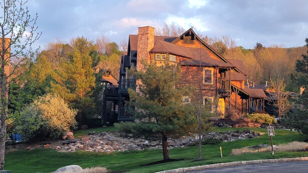 A large, rustic stone house with a prominent chimney, surrounded by a well-maintained lawn and trees. - Little Getaway at Mountain Creek Sanctuary (Vernon Township)
