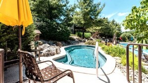 A hot tub surrounded by trees and a pool, with a chair and umbrella nearby. - Little Getaway at Mountain Creek Sanctuary (Vernon Township)