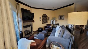 A living room with a fireplace, a sofa, a leather armchair, and a television. - Little Getaway at Mountain Creek Sanctuary (Vernon Township)