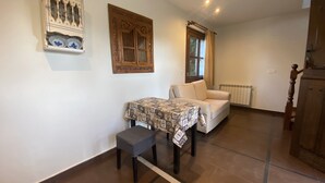 Ein Zimmer mit einem weißen Sofa, einem kleinen Tisch mit gemustertem Tuch, einem Holzschrank und einem Wanddekor.