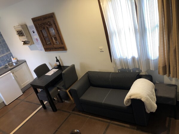 A modern living room with a dark sofa, a dining table, and a kitchen area with a sink and cabinets. - THE HOUSES OF MÍA 3 QUINTANA DE LLANES (LLANES)