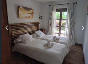 A room with two beds, a wooden headboard, a painting on the wall, and a window with curtains. - THE HOUSES OF MÍA 3 QUINTANA DE LLANES (LLANES)