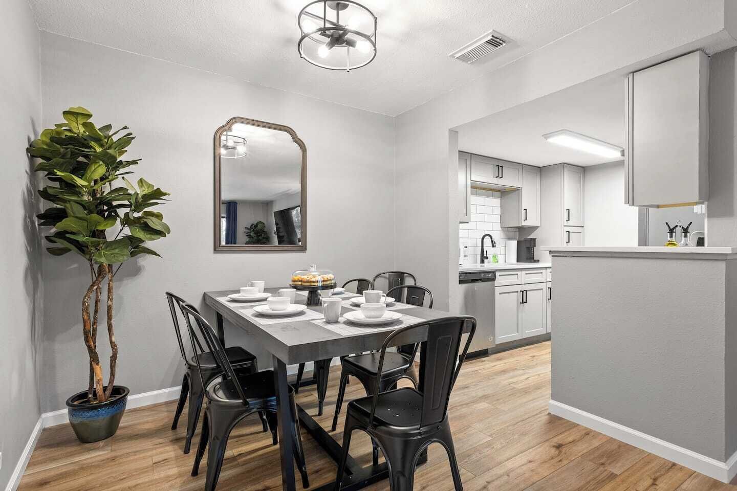 A modern kitchen with white cabinets, a dining area with a table set for four, and a potted plant.