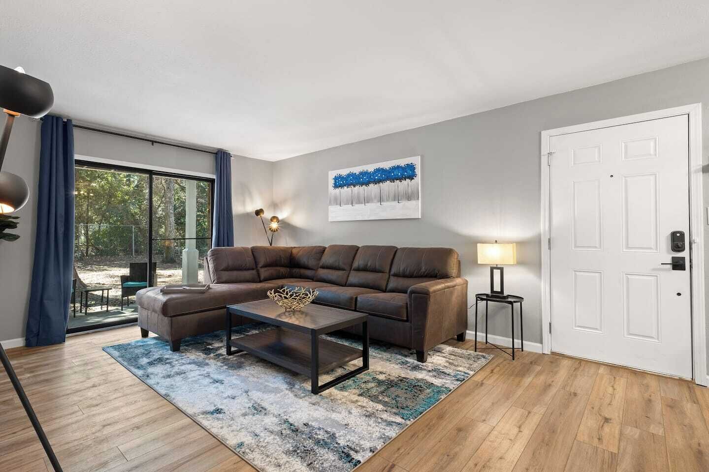 A modern living room with a brown leather sofa, a coffee table, and a large window with curtains.