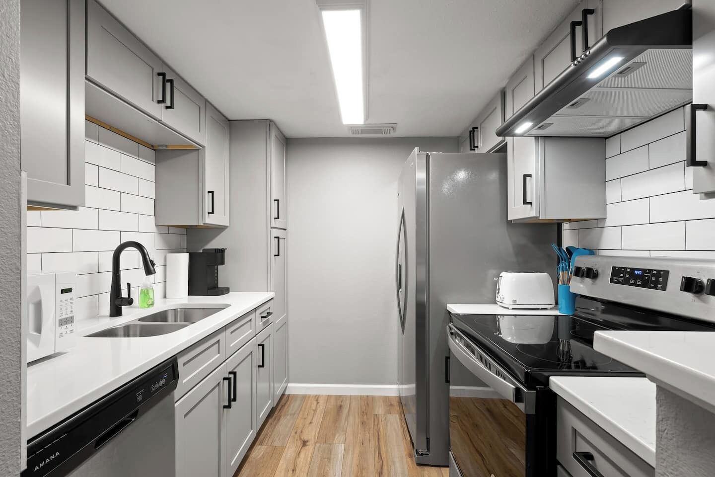 A modern kitchen with white cabinetry, stainless steel appliances, and a wooden floor.