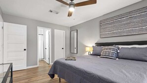 Un dormitorio con cama, ventilador de techo, mesita de noche y una obra de arte en la pared.