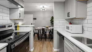 Una cocina compacta con armarios blancos, horno empotrado, microondas y lavaplatos.