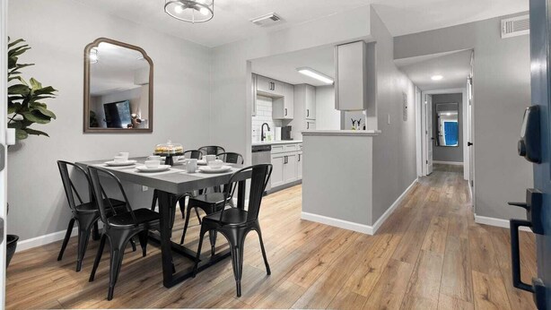 Una cocina moderna con armarios blancos, una isla central y una zona de comedor con mesa y sillas.