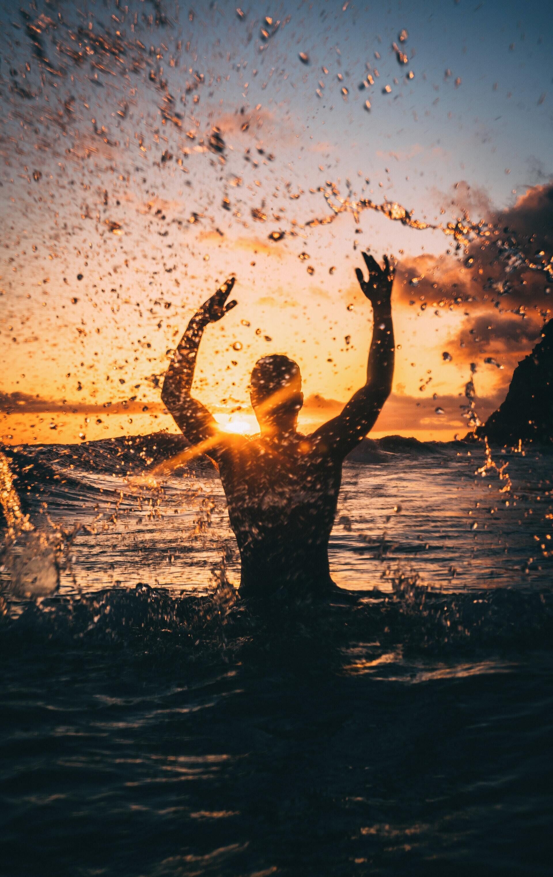 Eine Silhouette einer Person mit erhobenen Armen vor einem Sonnenuntergang.