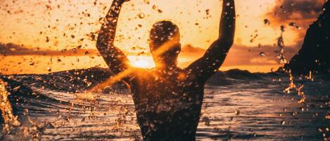Eine Silhouette einer Person mit erhobenen Armen vor einem Sonnenuntergang.