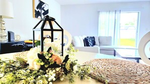 Sala de estar con sofá, una mesita de centro y una composición decorativa que incluye un farol y flores.