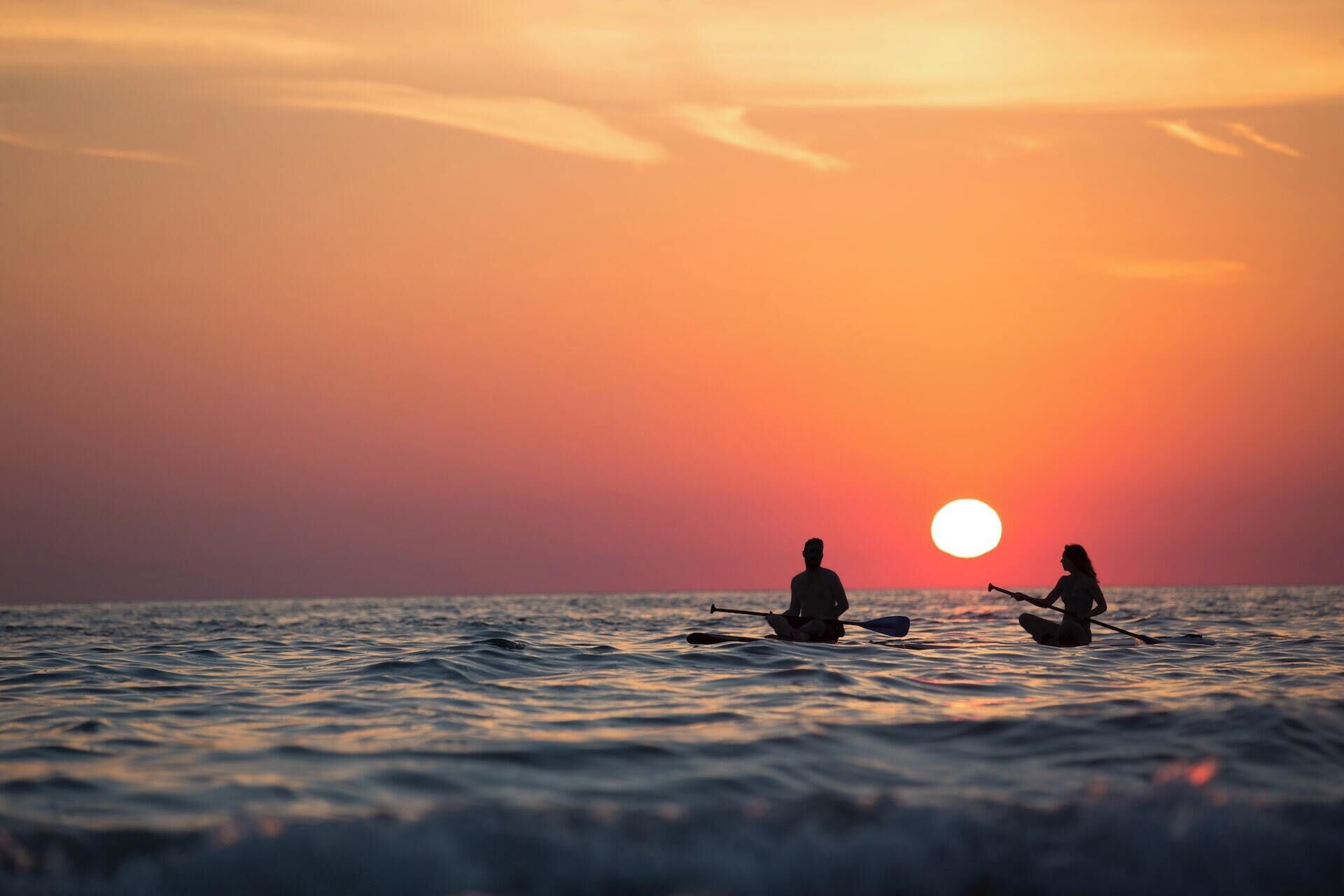 Dos personas remando en kayak en un cuerpo de agua durante el atardecer.