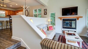 A modern living room with a staircase, a fireplace, and a television mounted above it.