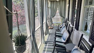 Relax on the covered porch with comfortable seating and a small table, surrounded by lush greenery and a beautiful outdoor view.