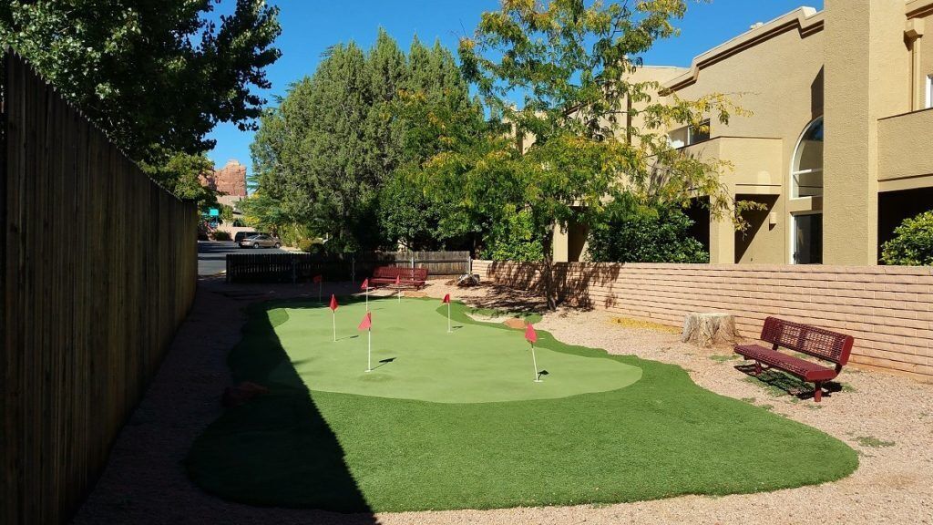 Un petit terrain de golf bien entretenu, avec une clôture en bois, un banc et des arbres en arrière-plan.