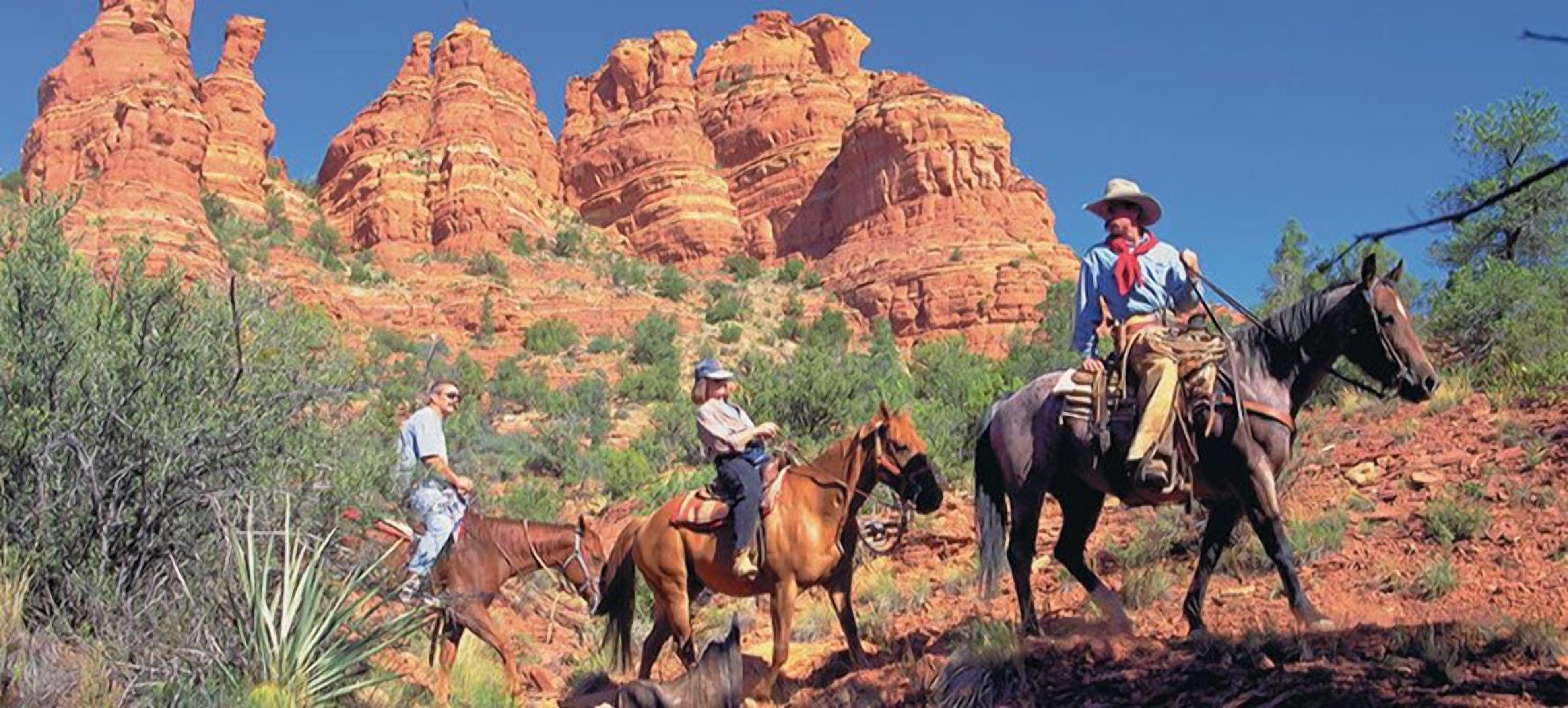 Eine Wüstenlandschaft mit roten Felsen und drei Personen, die zu Pferd reiten.
