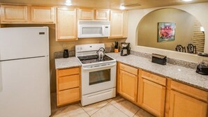 Cocina compacta con refrigerador, microondas, estufa y armarios de madera.