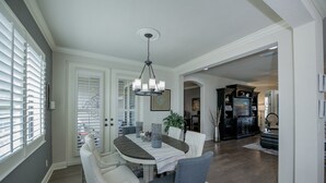 A dining area with a table, chairs, and a chandelier. There is a door leading to another room and a plant on the table.