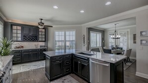 A modern kitchen with dark cabinetry, a marble island, and recessed lighting.