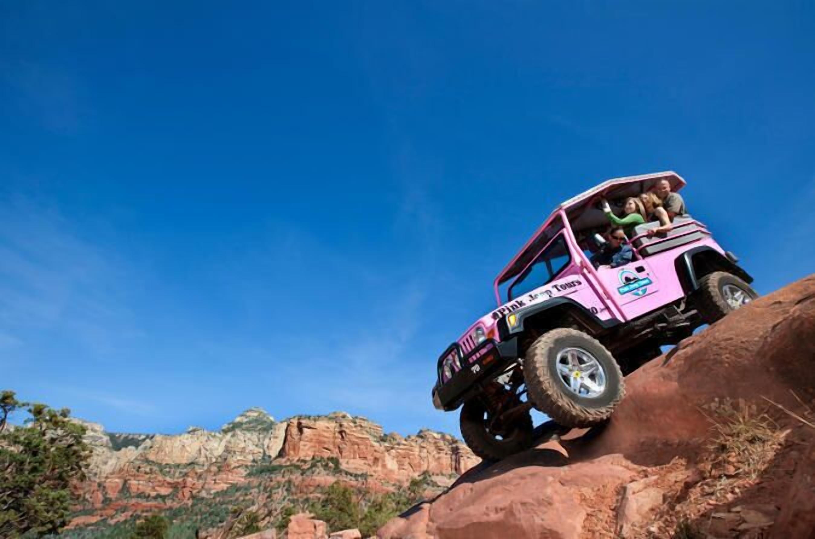 A pink off-road vehicle with passengers on a rocky terrain.