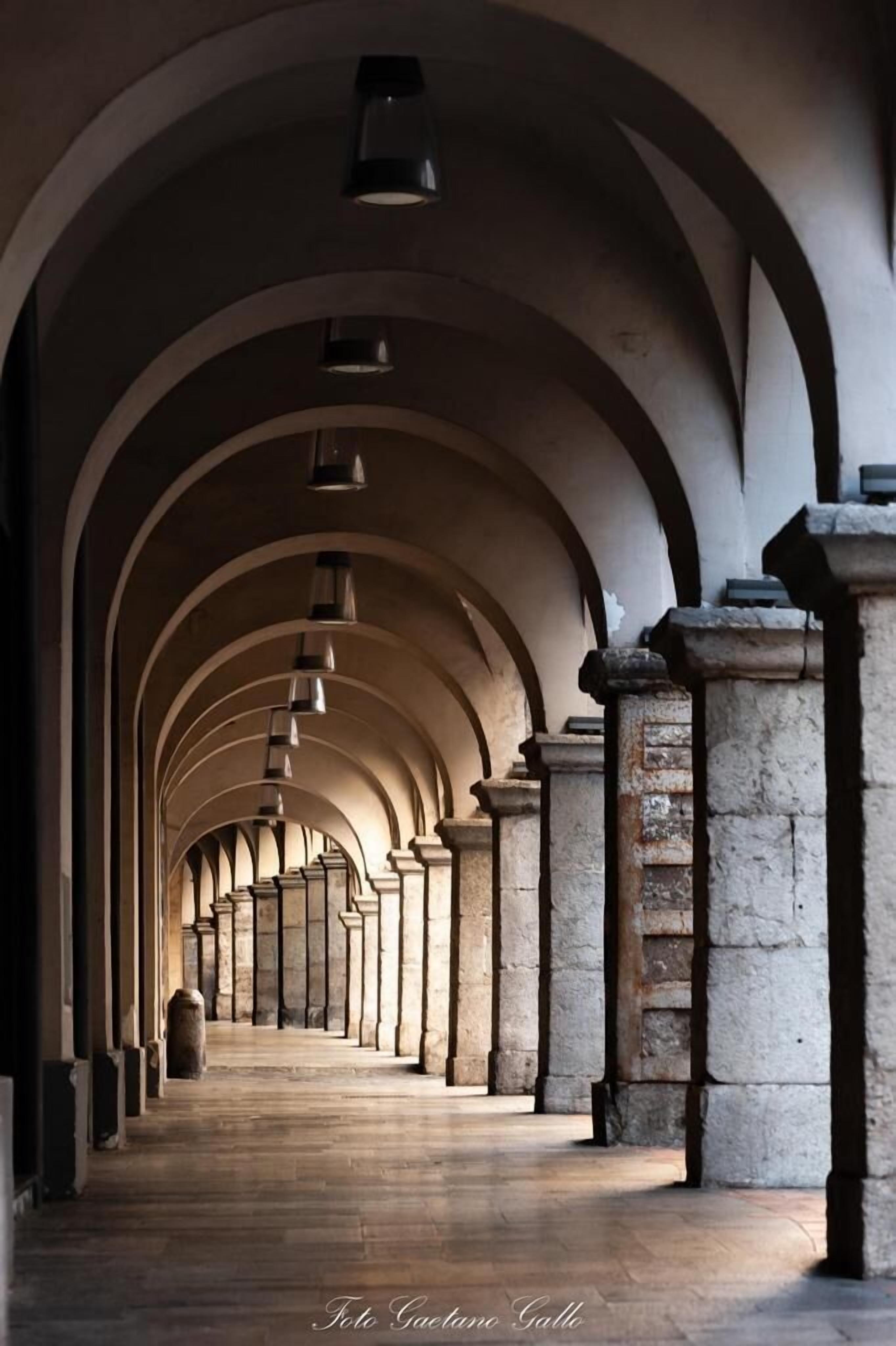 A corridor with a series of arches and columns, leading to a distant end.