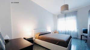 Een moderne hotelkamer met een bed, nachtkastje, lamp, televisie en een bureau met stoel.