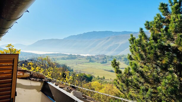 A balcony with a view of distant mountains, a pine tree, and a small garden with yellow flowers. - Rustic  Cottage by Gran Sasso: Steps away from Amazing Hiking Trails (Frascara)