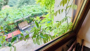 A window with a view of a garden, a wooden bench, and a red table outside. - Rustic  Cottage by Gran Sasso: Steps away from Amazing Hiking Trails (Frascara)