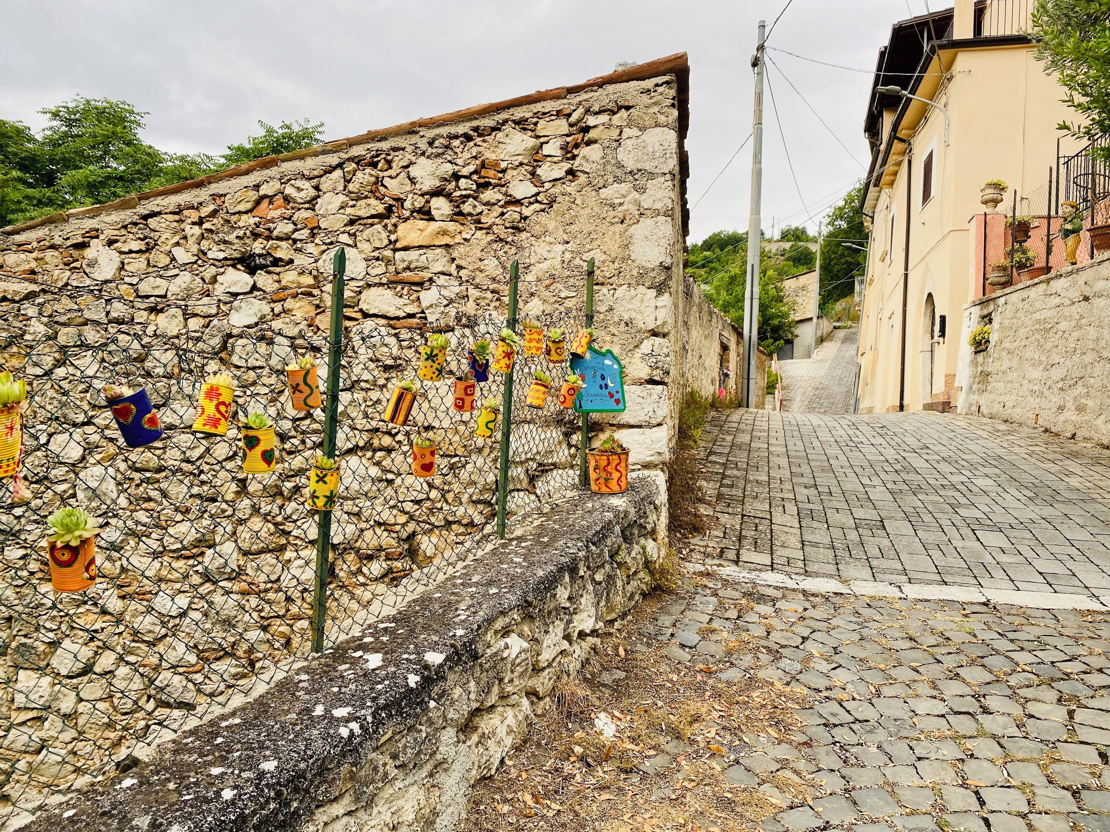 Eine gepflasterte Straße, an einer Seite eine Steinmauer, auf der anderen Seite ein Gebäude.