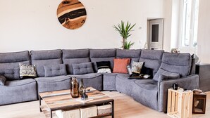 Una sala de estar moderna con un sofá seccional gris, una mesa de centro de madera y una mesita auxiliar de madera.