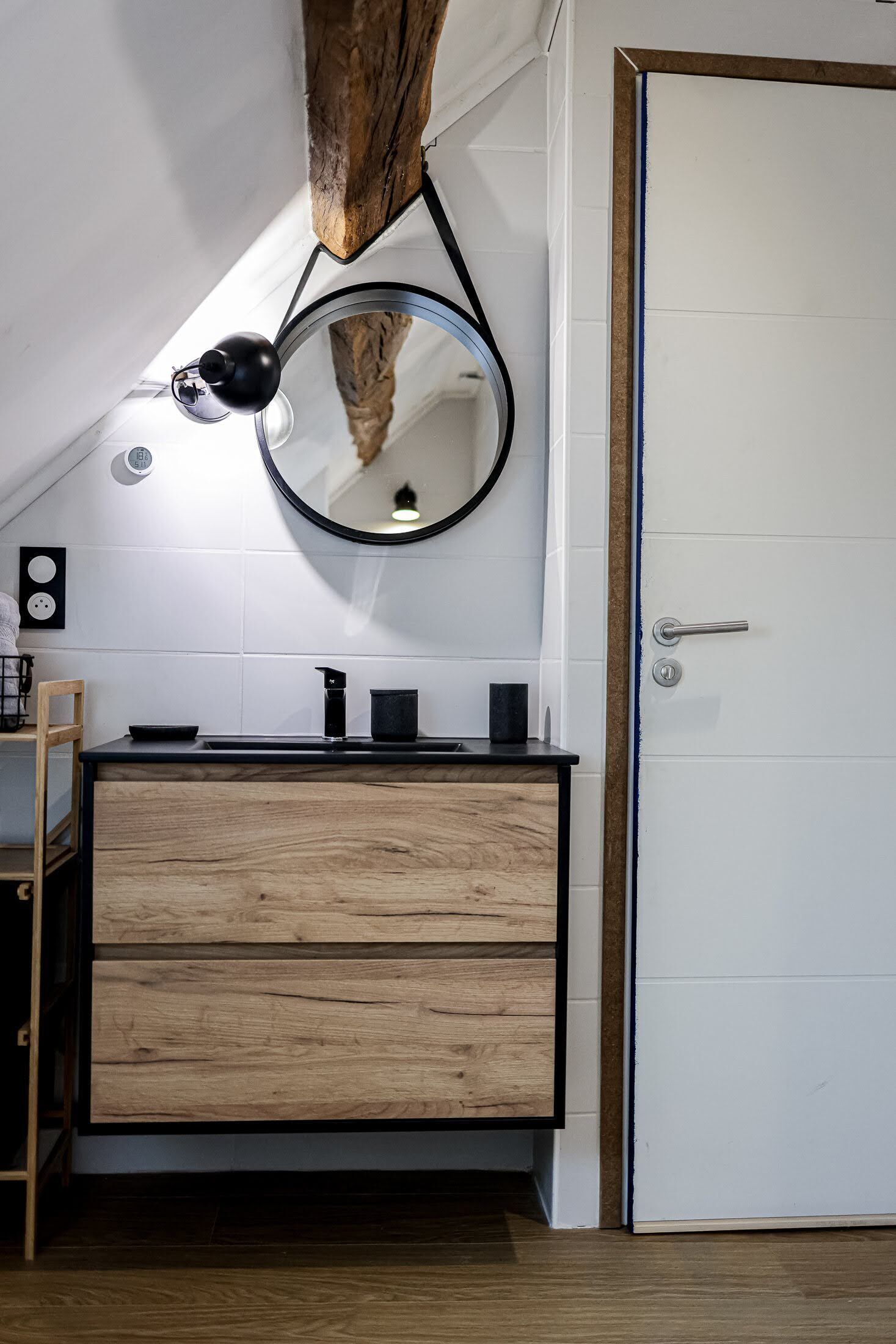Un baño moderno con tocador de madera, un espejo redondo y una lámpara colgante.