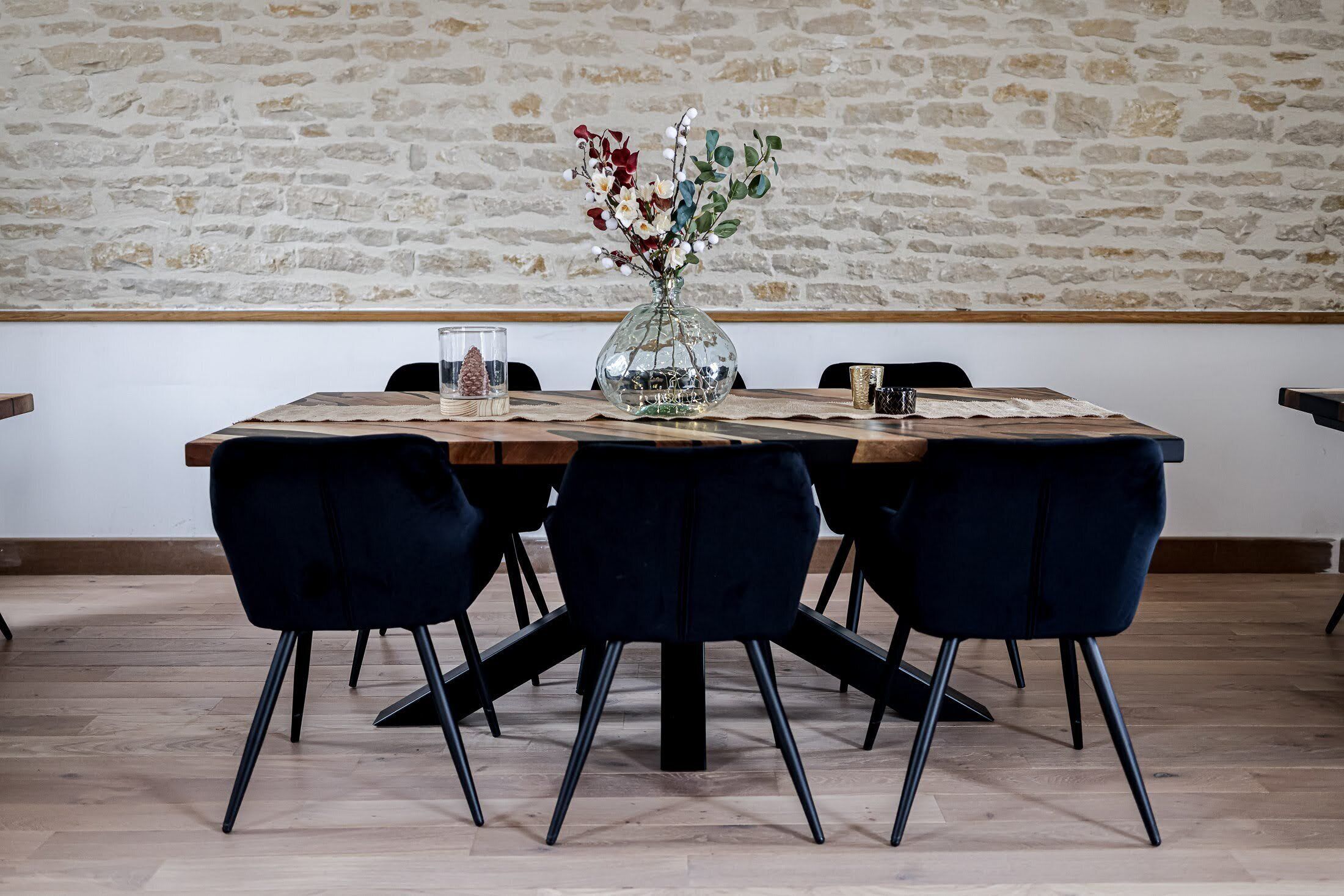 A dining table with a glass vase of flowers, dark chairs, and a wooden table runner.