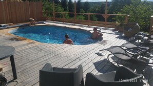 Una terraza de madera con piscina, rodeada por una valla de madera y árboles.
