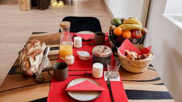 A breakfast setup with bread, fruit, and beverages on a wooden table with a red placemat.