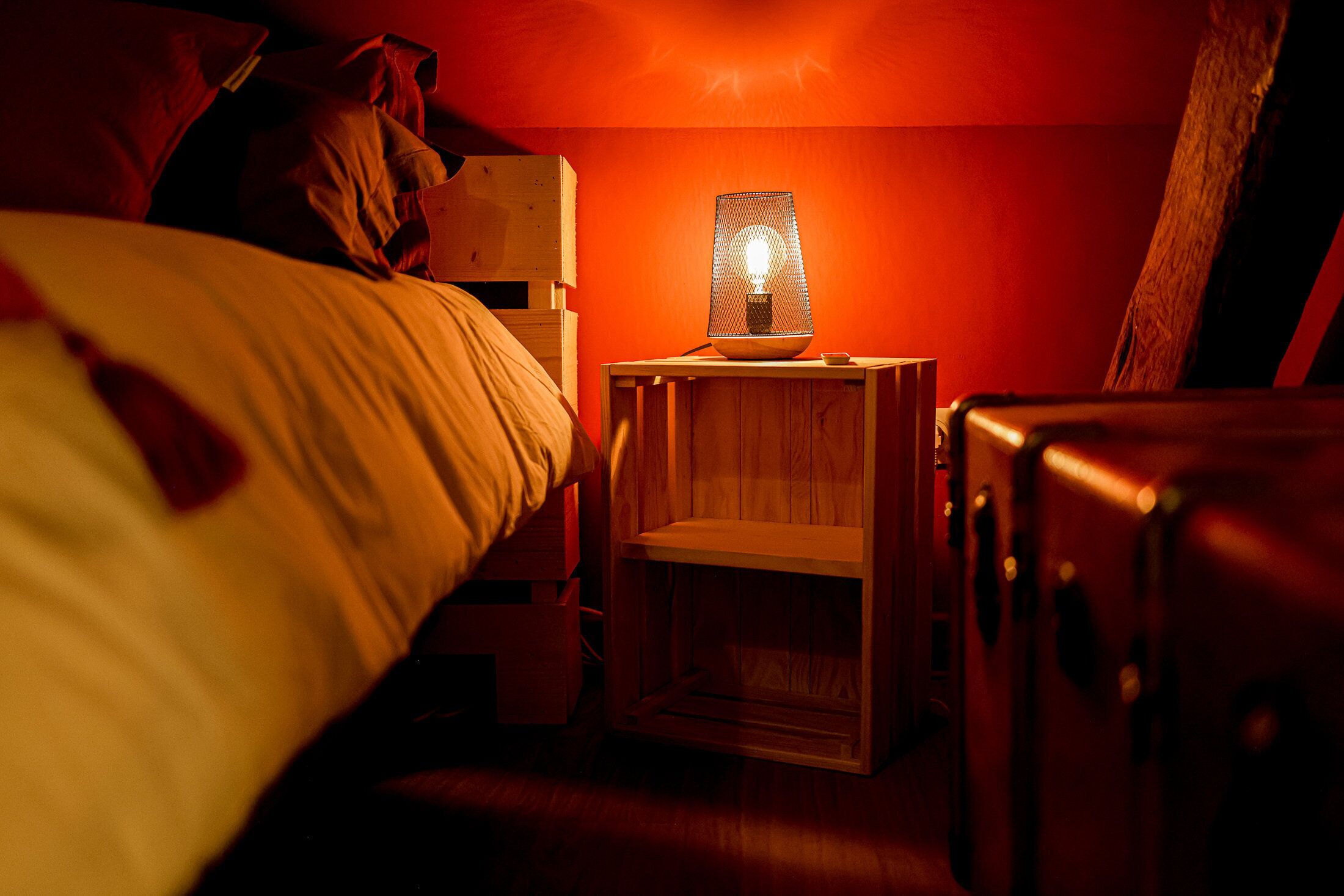 A dimly lit room with a wooden nightstand, a lamp, and a suitcase.
