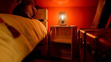 Una habitación tenuemente iluminada con una mesita de noche de madera, una lámpara y una maleta.