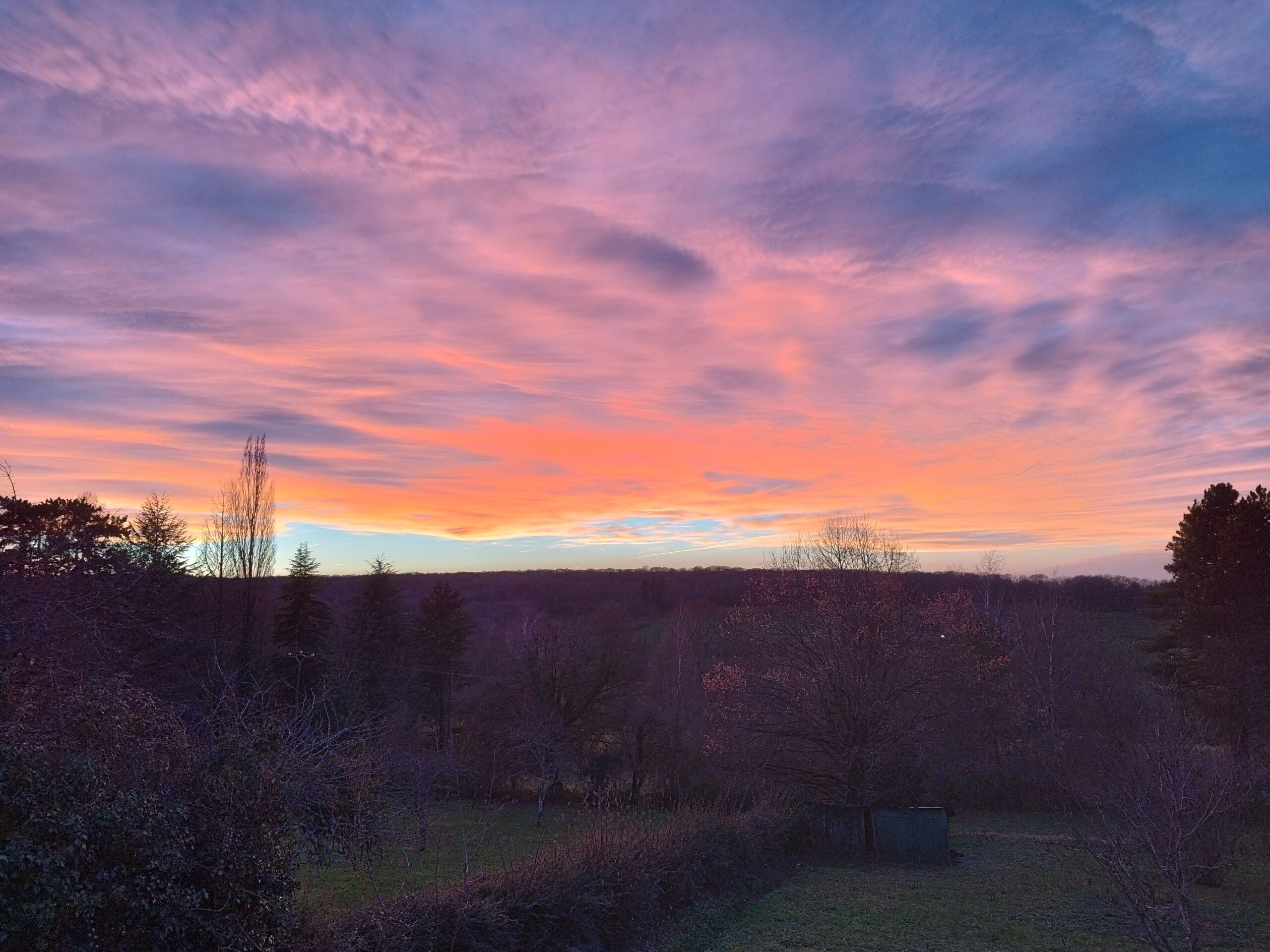 Un paisaje natural con un cielo al atardecer, árboles y una construcción pequeña.