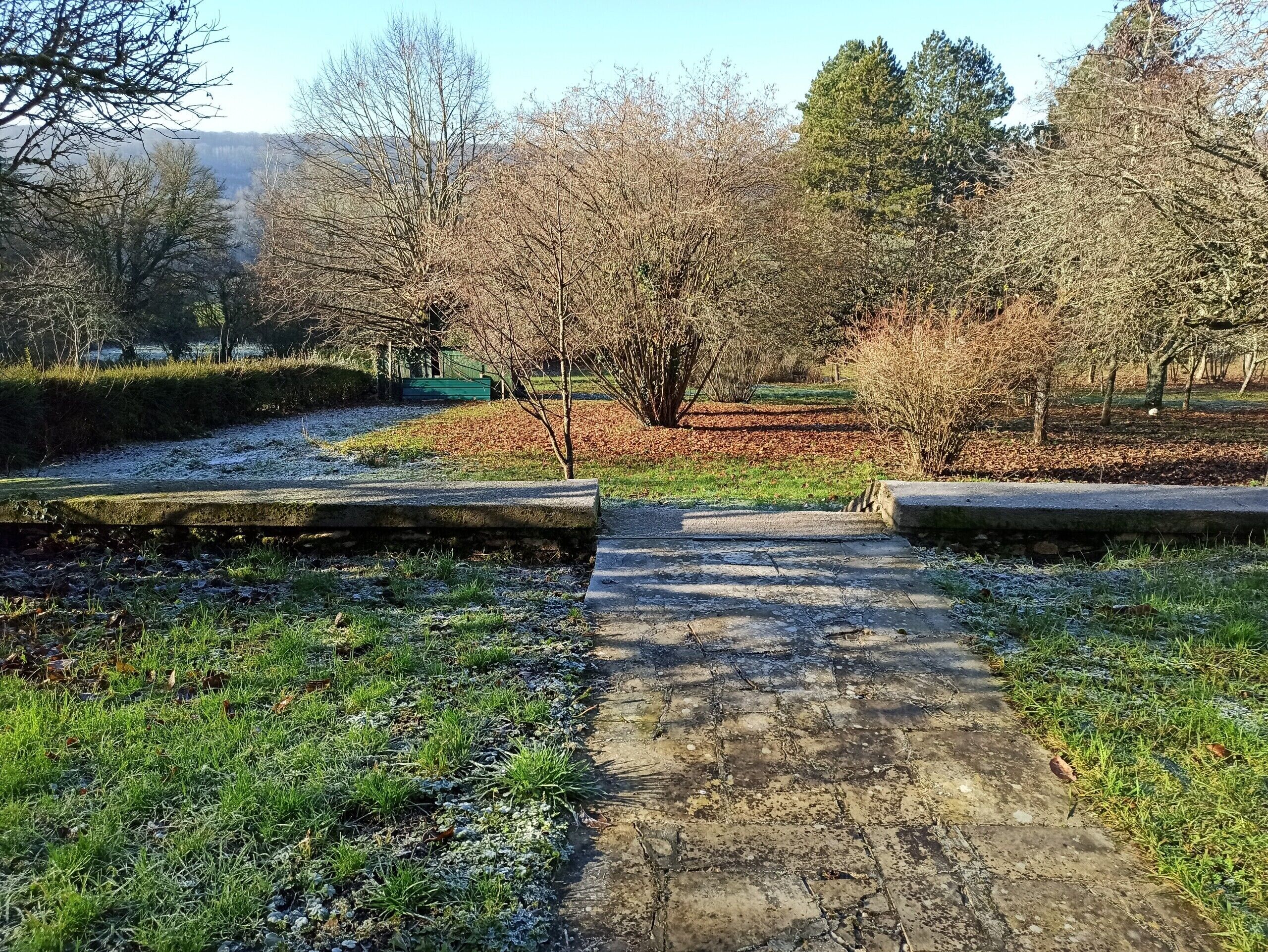 A pathway leading through a park with trees and a distant view of hills.