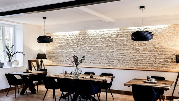 Comedor con pared de piedra, mesa de madera, sillas negras y lámparas colgantes.