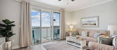 A spacious living room with a large sliding glass door leading to a balcony, a ceiling fan, a sofa set, and a coffee table.