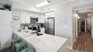 Una cocina moderna con armarios blancos, una isla grande con taburetes, un refrigerador de acero inoxidable y un microondas.