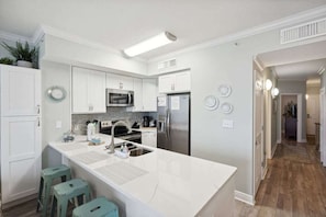 Una cocina moderna con armarios blancos, una isla grande con taburetes, un refrigerador de acero inoxidable y un microondas.