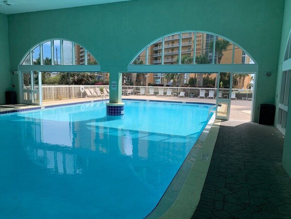 An indoor swimming pool with clear glass walls, a tiled floor, and a 'KEEP OFF' sign.