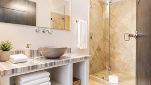 Ein Badezimmer mit einem großzügigen Marmorwaschbecken, einem Spiegel, einer Dusche und einem Handtuchhalter.