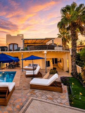 A poolside area with lounge chairs, umbrellas, and a stone-tiled patio.