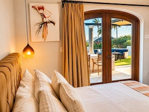 A bedroom with a bed, a hanging light fixture, a door leading to an outdoor area, and a wall-mounted artwork.