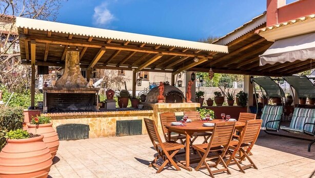 Un patio al aire libre con chimenea de piedra, mesa y sillas de madera, y plantas en macetas.