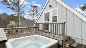 Un bain à remous sur une terrasse en bois, avec une balustrade blanche et des marches menant à une maison dotée d’une fenêtre.