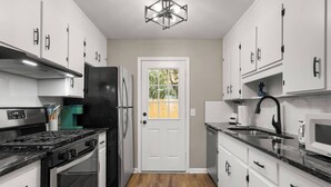 Una cocina moderna con armarios blancos, estufa negra, refrigerador de acero inoxidable y piso de madera.