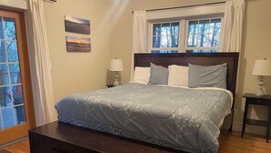Un dormitorio con cama, mesitas de noche, un banco, una ventana y una puerta.